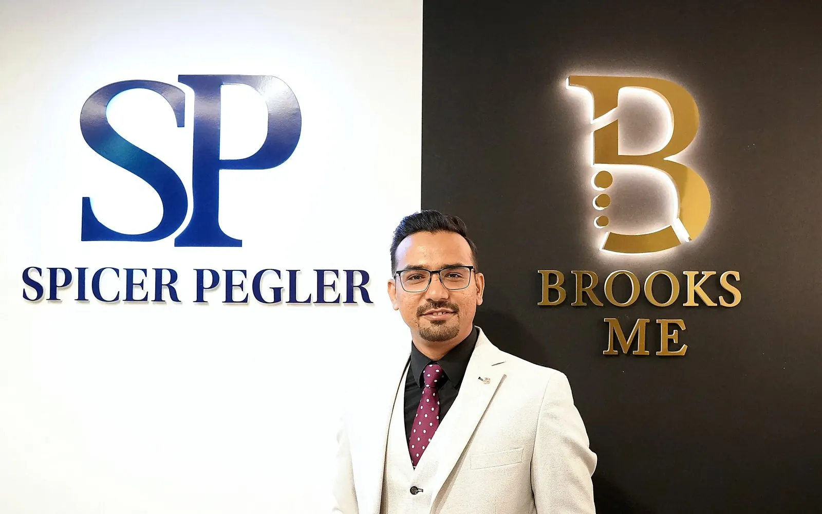 Mazahir standing between the Spicer Pegler and Brooks ME logo walls.