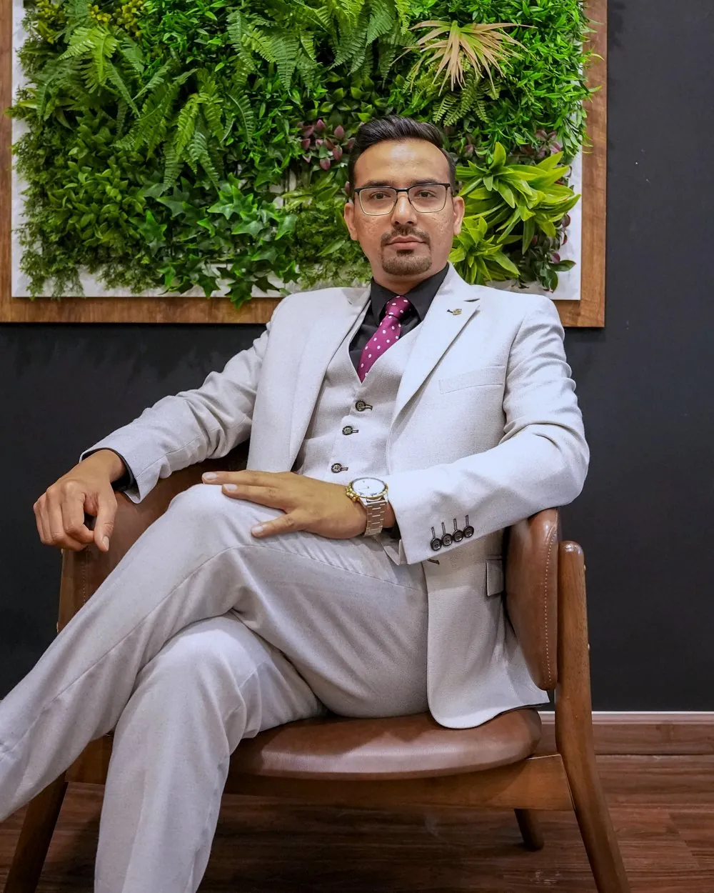 Mazahir seated in a leather chair in front of a living plant wall.